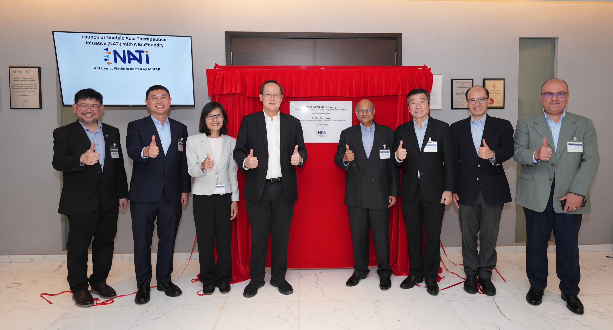 Group photo of A*STAR leadership and guests, including Dr Tan Lee Seng (Minister for Manpower and Second Minister for Trade and Industry), at the launch of the NATi mRNA BioFoundry, with participants giving a thumbs-up gesture in front of the unveiling plaque